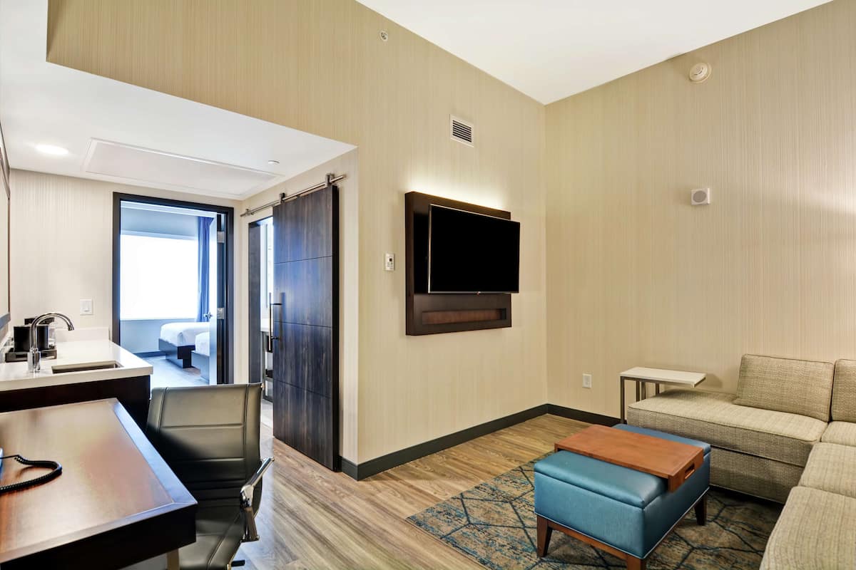 Une chambre d’hôtel comprenant un lit, un bureau avec une chaise, un téléviseur fixé au mur, un canapé et une petite table.