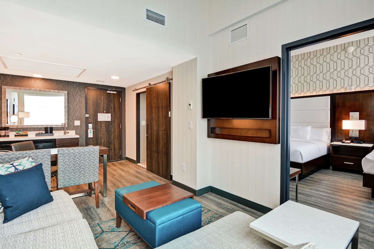 Une chambre d’hôtel comprenant un lit, une télévision, un bureau avec une chaise et un coin salon avec un canapé et un pouf.