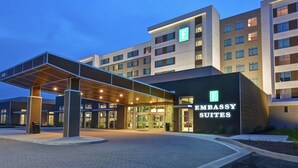 A modern building with a prominent "Embassy Suites" sign, featuring a covered entrance and multiple floors.