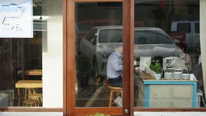 A hotel entrance with a wooden door, a signboard, and a reflection of a parked car and a person inside.