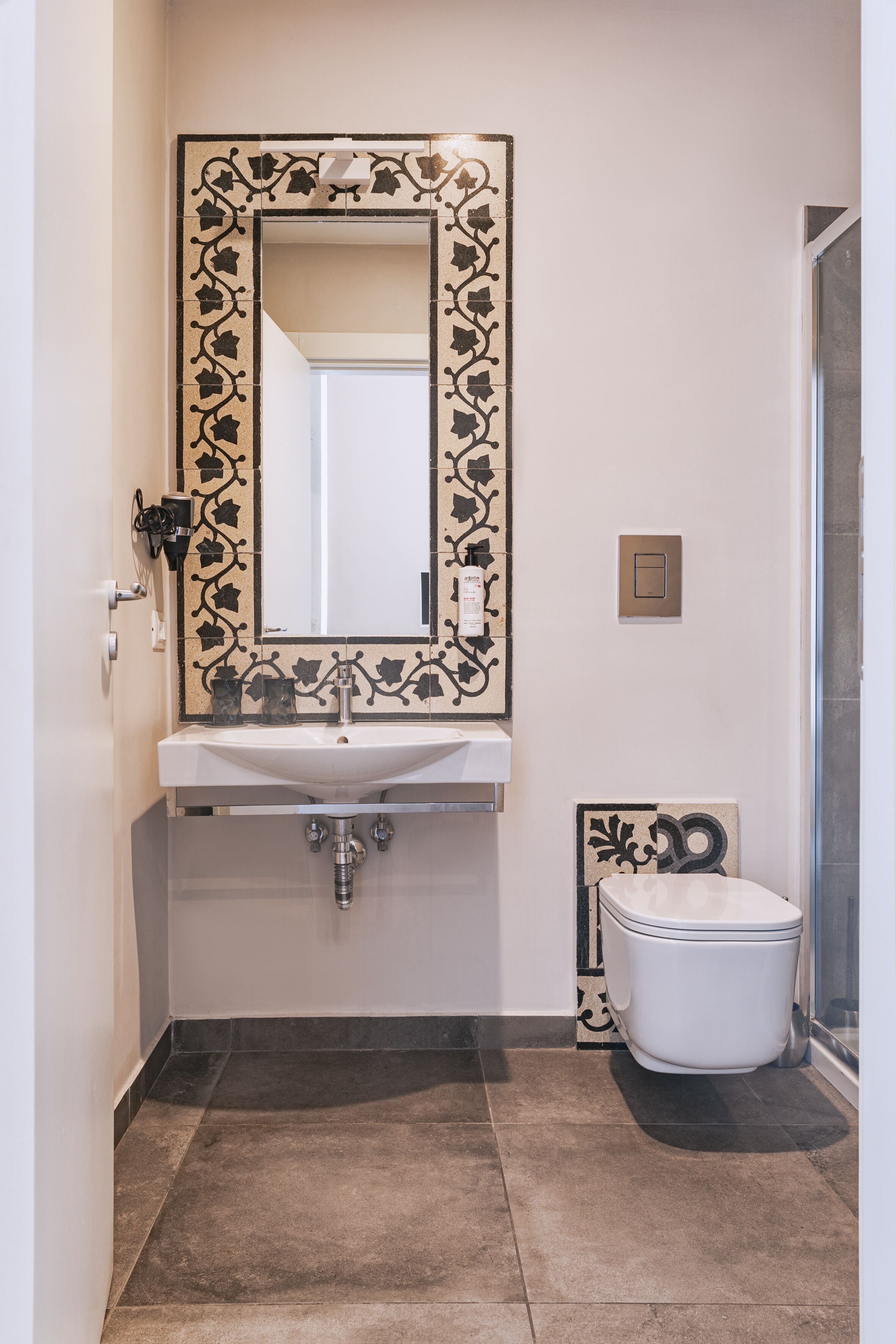 A bathroom with a white sink, a mirror with a decorative frame, a toilet, and a shower area.
