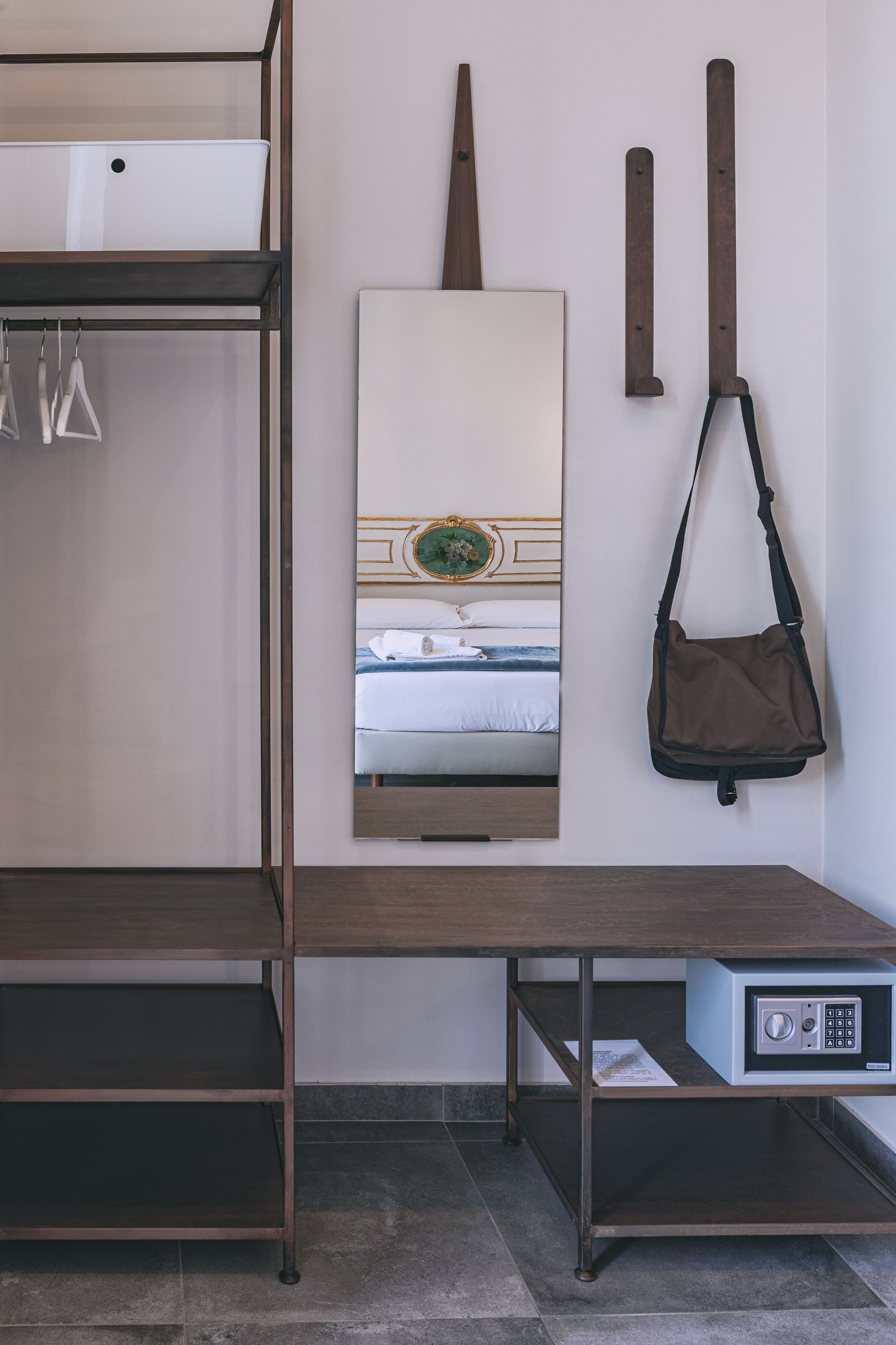 Una cama litera con escritorio y caja fuerte, un cuadro de una cama y un bolso colgado.