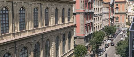 Vista da rua com edifícios históricos, carros estacionados e árvores.