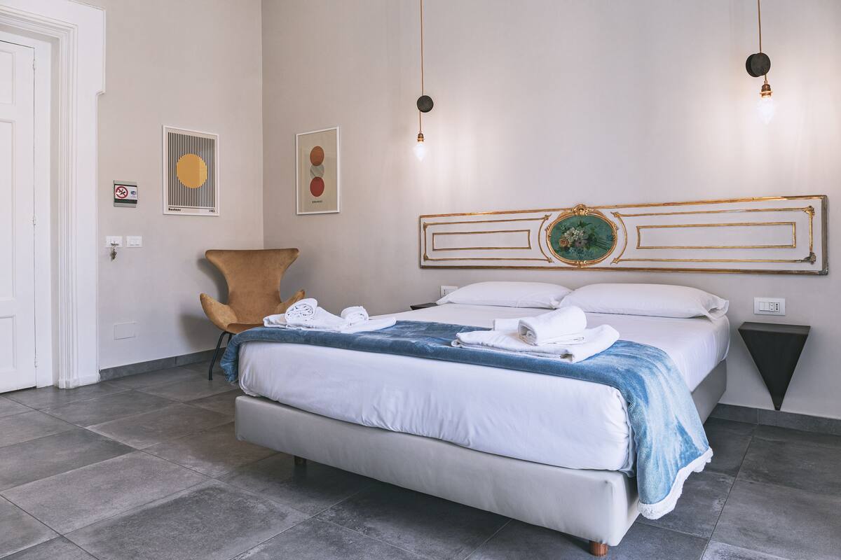 A neatly arranged bedroom with a bed, a chair, and a wall-mounted artwork.