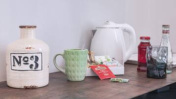 Un ripiano da cucina con una teiera bianca, una tazza verde, un brocchetta bianca, una bottiglia rossa, una bottiglia trasparente e una confezione di tè.