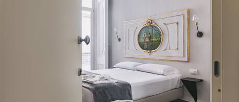 A bedroom with a bed, a bedside table, a wall-mounted picture frame, and a window.