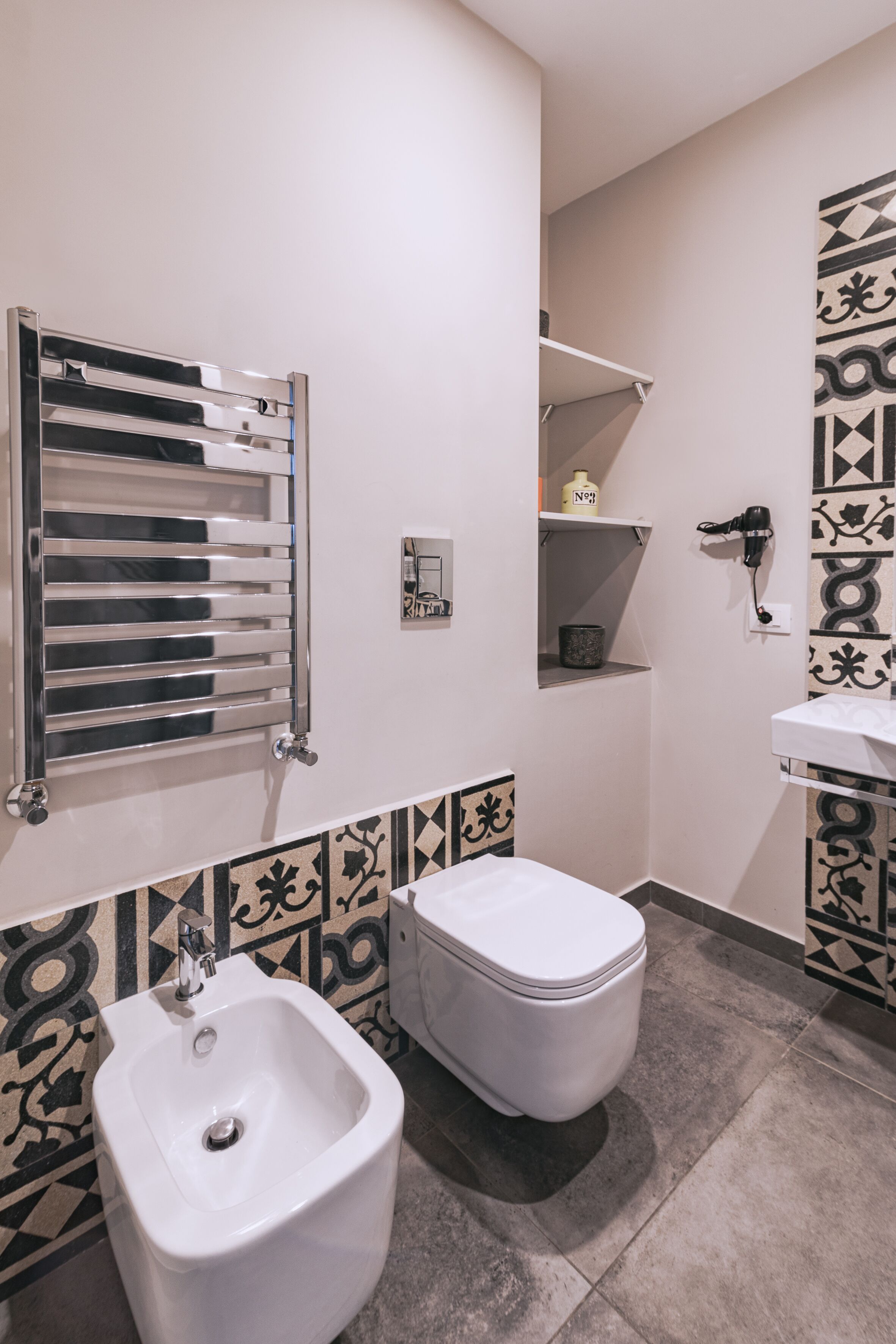 A bathroom with a bidet, a toilet, a towel rack, and a shelf with toiletries.