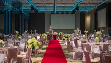A banquet hall with a red carpet aisle, rows of tables with white tablecloths, and floral centerpieces.
