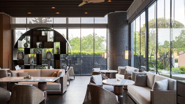 A modern lounge area with seating arrangements, a central table, and large windows offering a view of greenery. - Renaissance Taipei Shihlin Hotel (Taipei)