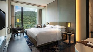 A modern hotel room with a large bed, a desk, and a view of a forested hill. - Renaissance Taipei Shihlin Hotel (Taipei)