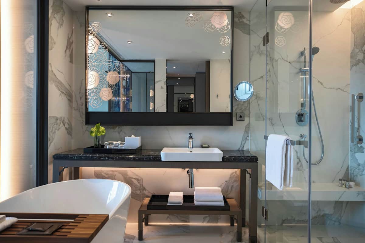 Un baño moderno con un espejo grande, una bañera, ducha con mampara de vidrio y encimera de mármol.