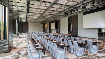 A conference room with rows of tables and chairs, a stage, and a large screen.