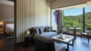 A modern hotel room with a sofa, armchairs, a coffee table, and a view of a forested landscape through large windows. - Renaissance Taipei Shihlin Hotel (Taipei)