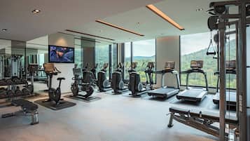 Un gimnasio moderno con diversos equipos de ejercicio, ventanas amplias y una pantalla de televisión.