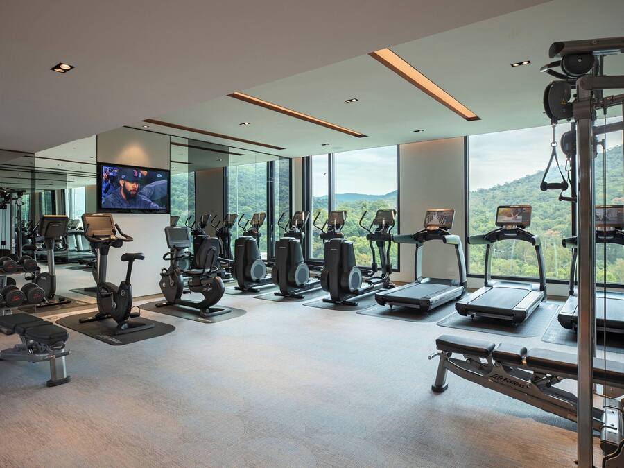Un gimnasio moderno con diversos equipos de ejercicio, ventanas amplias y una pantalla de televisión.