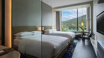 A hotel room with two beds, a TV, a desk, and a view of a mountainous landscape.