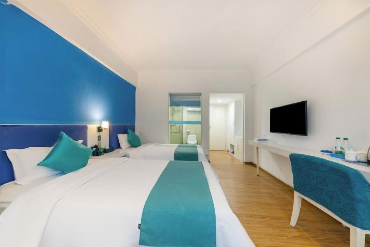 A hotel room with two beds, a TV, a desk, and a bathroom visible in the background.