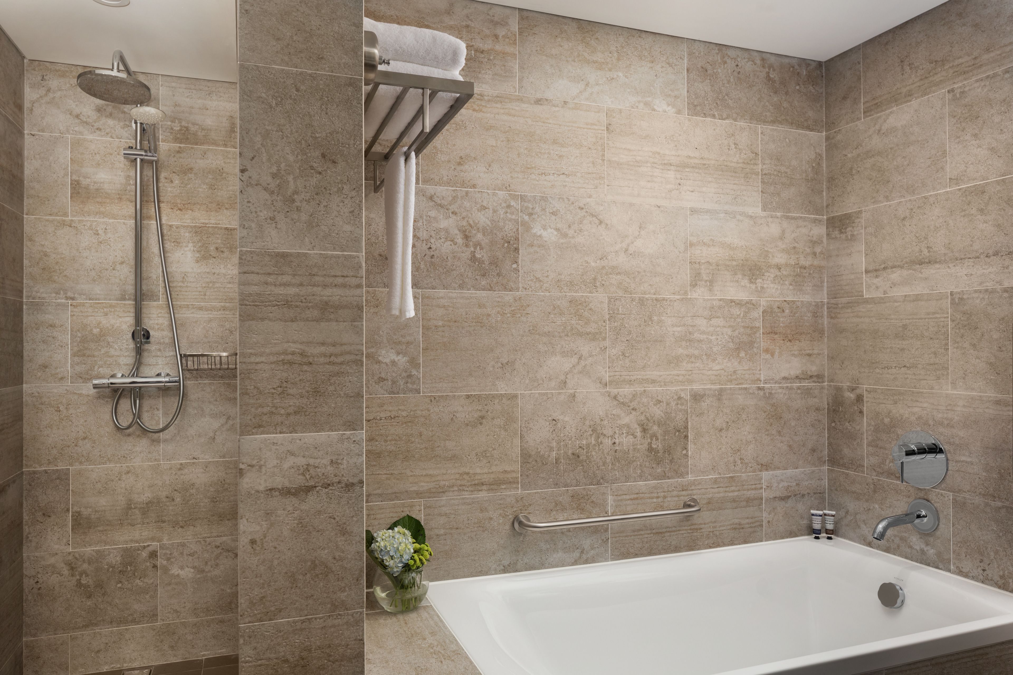 A modern bathroom with a bathtub, shower, and handrails.
