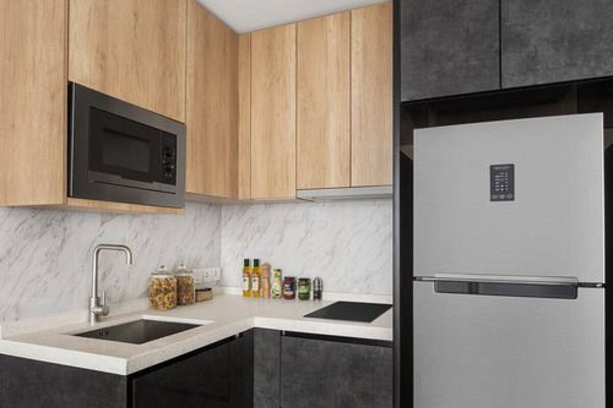 Eine moderne Küche mit Holzausstattung, einem Edelstahlkühlschrank, einer Mikrowelle und einem Waschbecken mit Marmorarbeitsplatte.