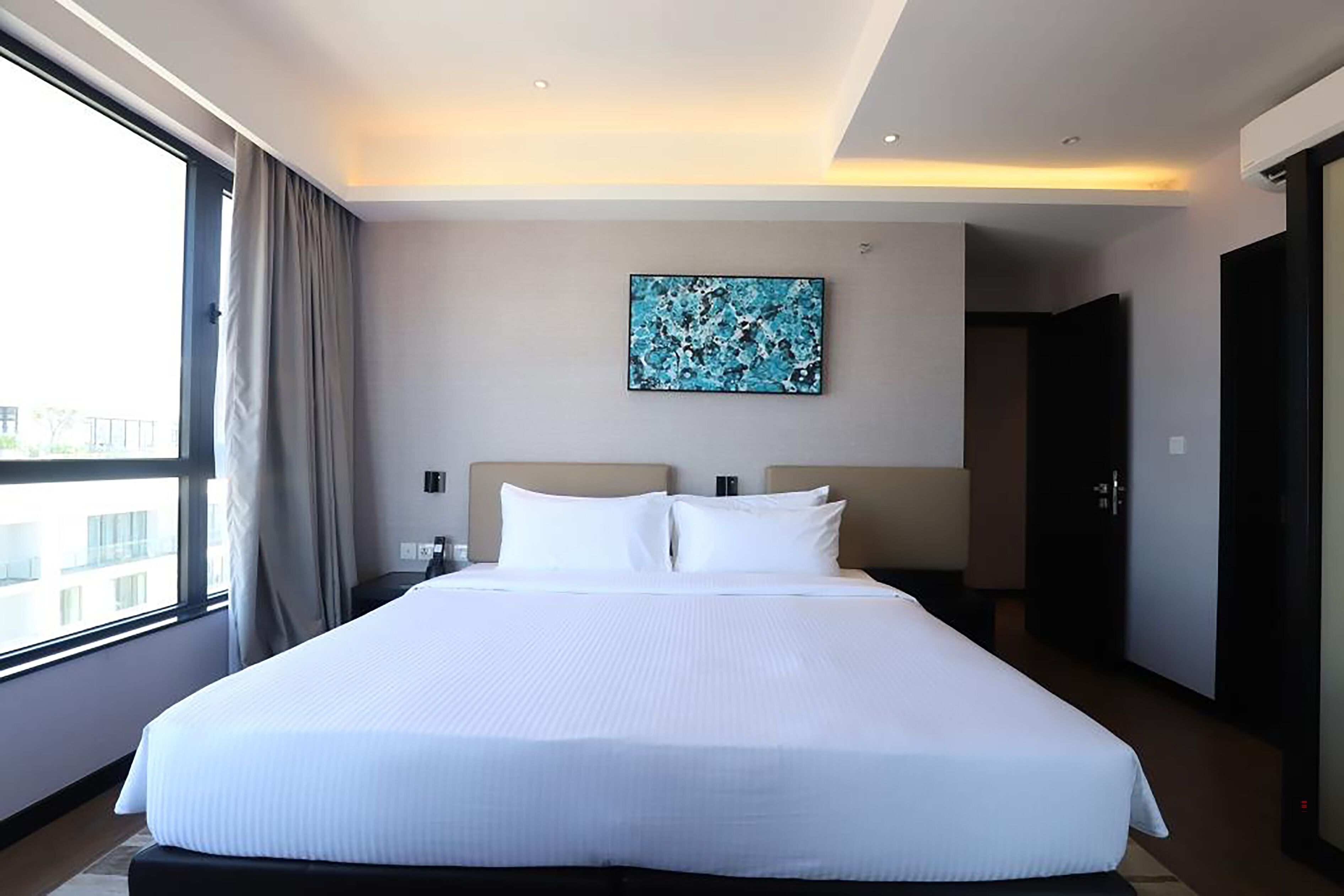 A hotel room with a large bed, a painting on the wall, and a view through the window.
