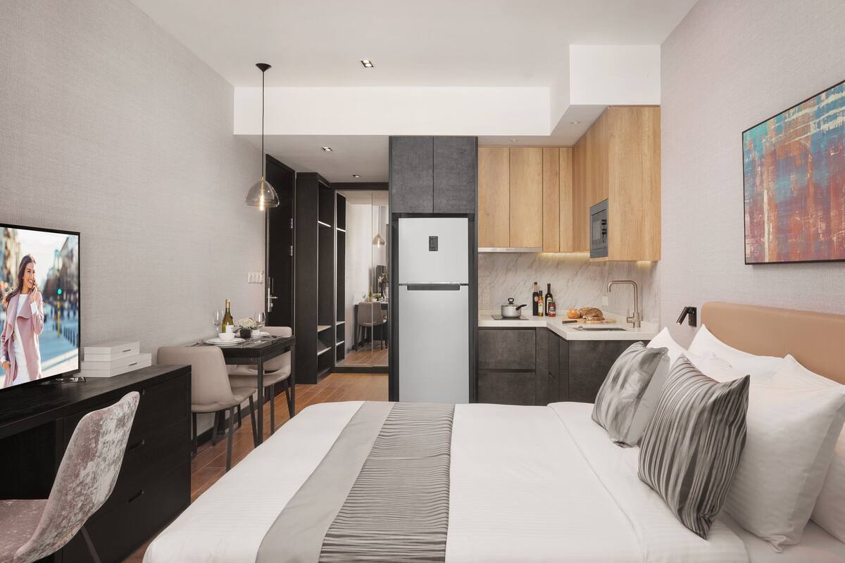 Ein modernes Hotelzimmer mit einem großen Bett, einem Schreibtisch, einem Stuhl, einem Fernseher, einer Küchenzeile und einem Esstisch.