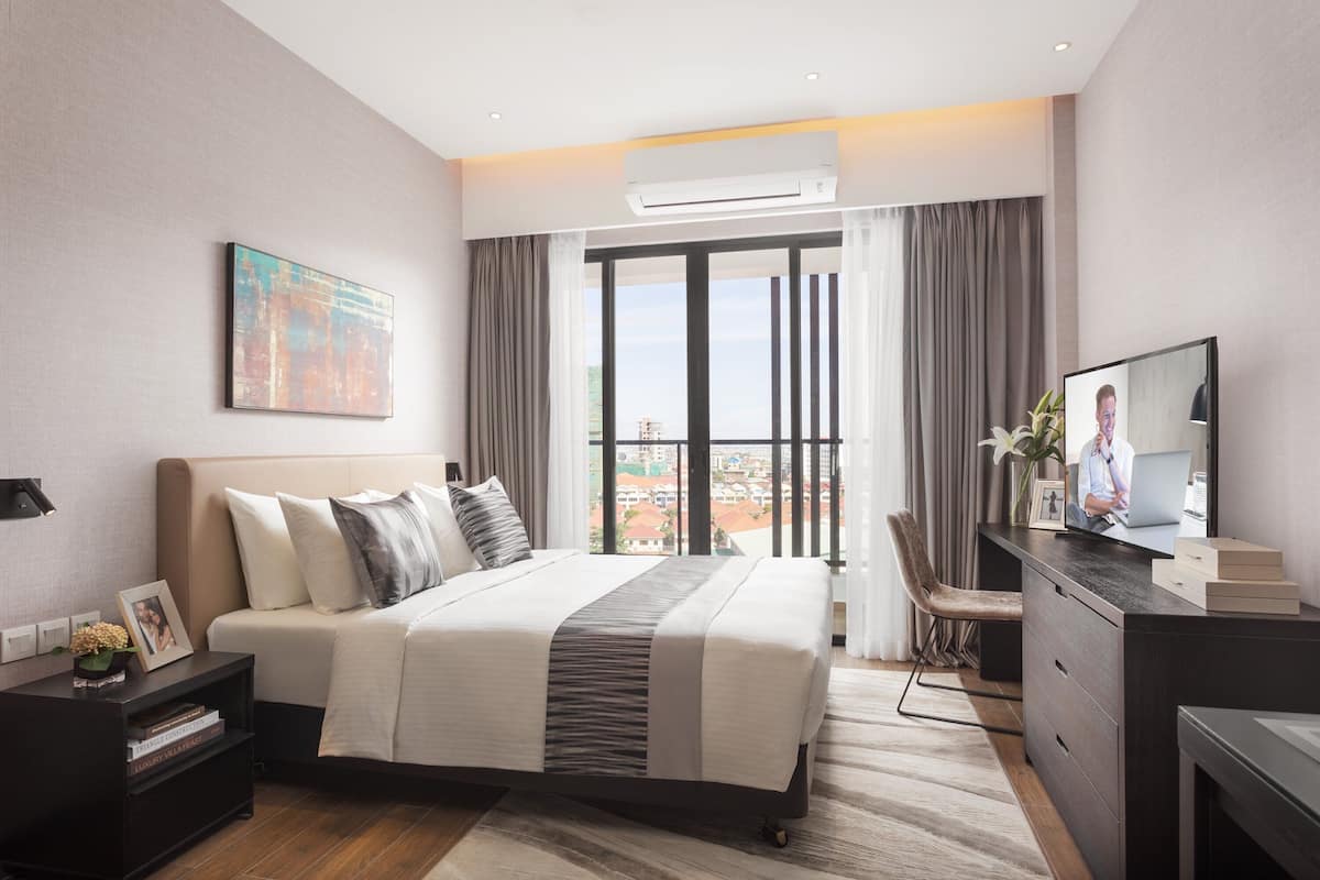 Ein modernes Hotelzimmer mit einem großen Bett, einem Schreibtisch mit einem Laptop, einem Fernseher und Blick auf die Stadt durch das Fenster.