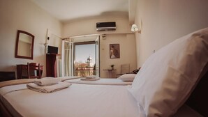 Habitación de hotel con cama, escritorio, silla, televisor y ventana con vista a un edificio.