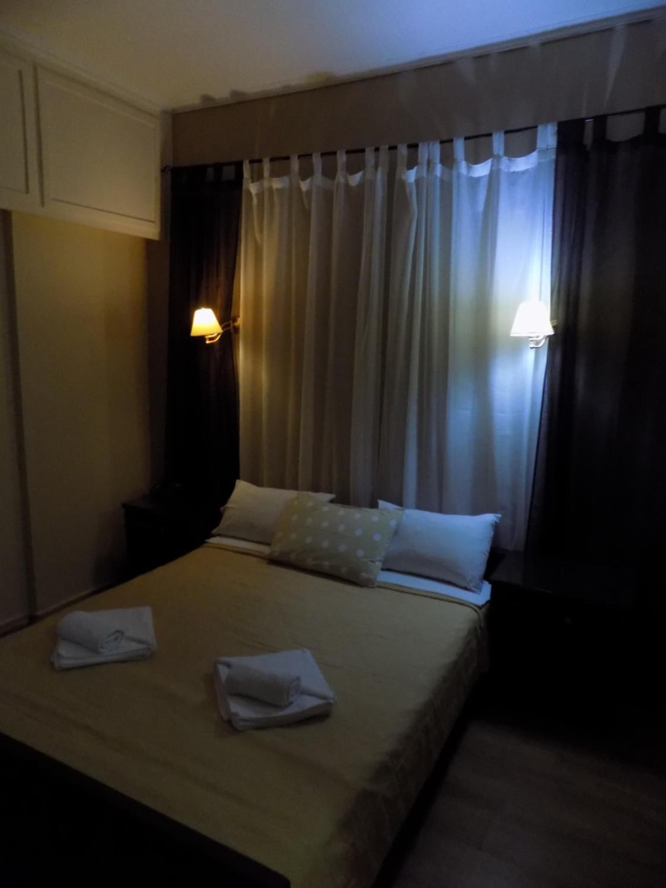Una habitación de hotel con cama, almohadas, una mesita de noche y una lámpara.