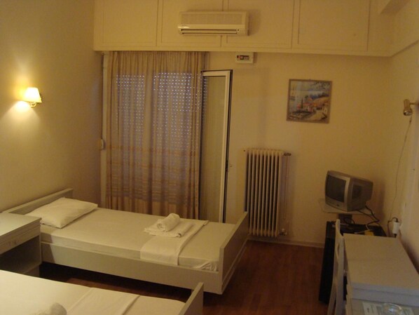 A hotel room with a single bed, a bedside table, a TV, and a radiator. - King Pyrros (Ioannina)