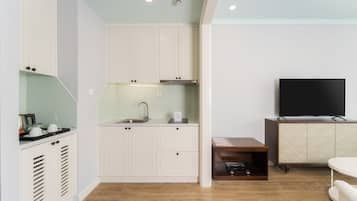 A compact kitchen with white cabinets, a sink, and a countertop with a kettle.