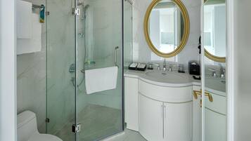A modern bathroom with a glass-enclosed shower, a white sink with gold handles, and a large mirror with a gold frame.