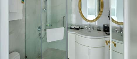 A modern bathroom with a glass-enclosed shower, a white sink with gold handles, and a large mirror with a gold frame.
