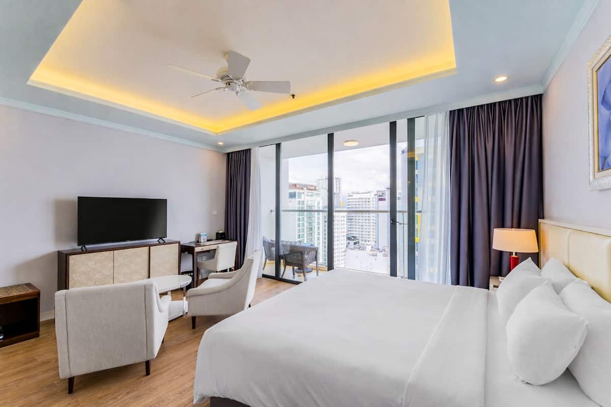 Hotelkamer met een bed, bureau, televisie en een balkon met uitzicht over de stad.
