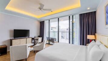 A hotel room with a bed, desk, TV, and a balcony with a city view.