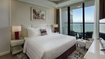 Habitación de hotel con una cama grande, un escritorio, una silla, un televisor, un teléfono, una lámpara, un cuadro y vistas al océano.