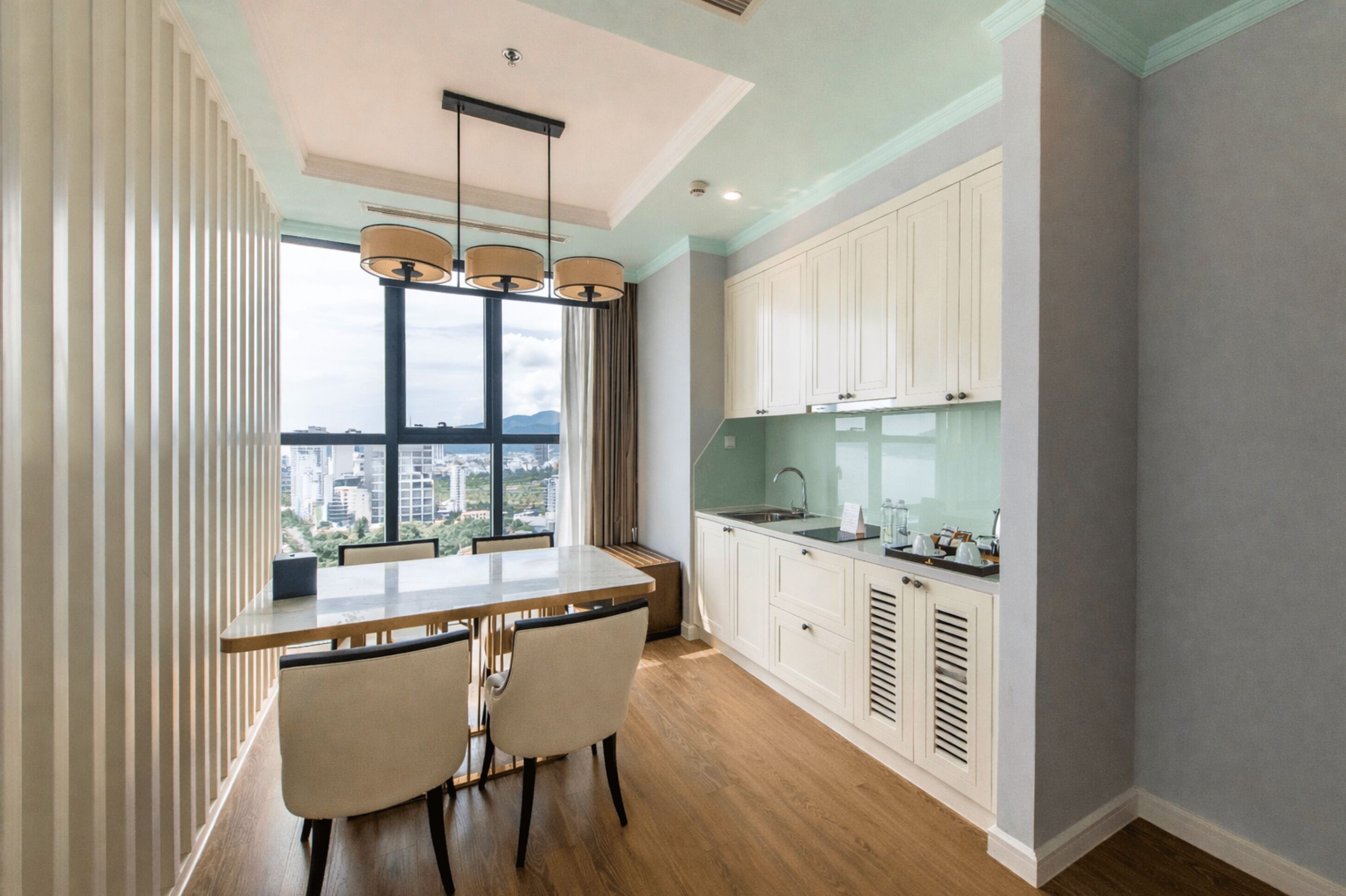 Una cocina moderna con un ventanal grande, un comedor con mesa y sillas, y armarios blancos.