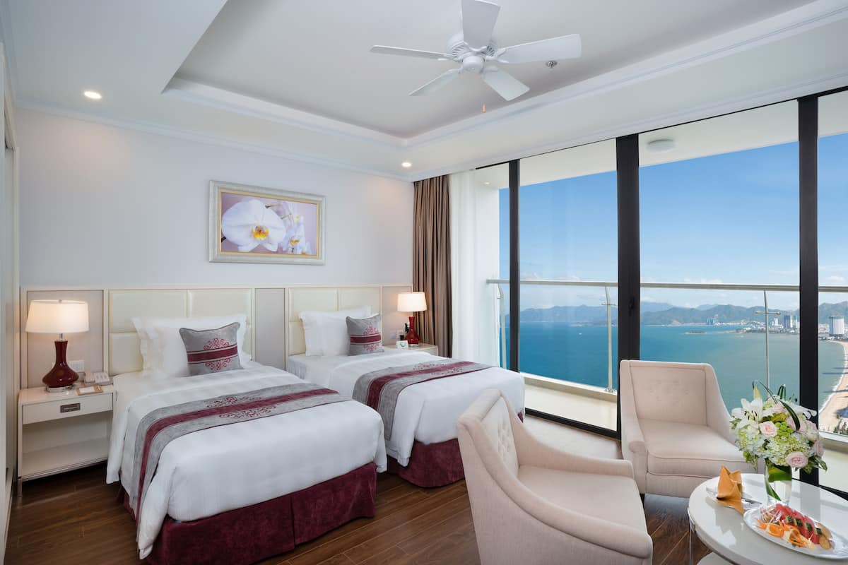 Een hotelkamer met twee bedden, een zithoek, een balkon met uitzicht op zee en een plafondventilator.