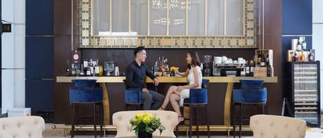 Un área de bar con dos taburetes, una mesa redonda con un florero y una zona de estar con dos sillones.