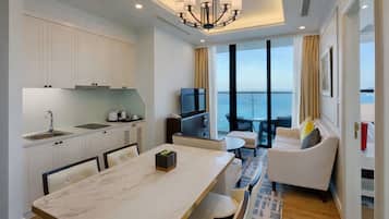 A modern hotel room with a kitchen, dining area, and a balcony with a view of the sea.