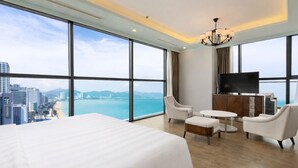 Une chambre d’hôtel dotée d’un grand lit, d’une télévision, d’un coin salon et offrant une vue sur la ville et la mer.