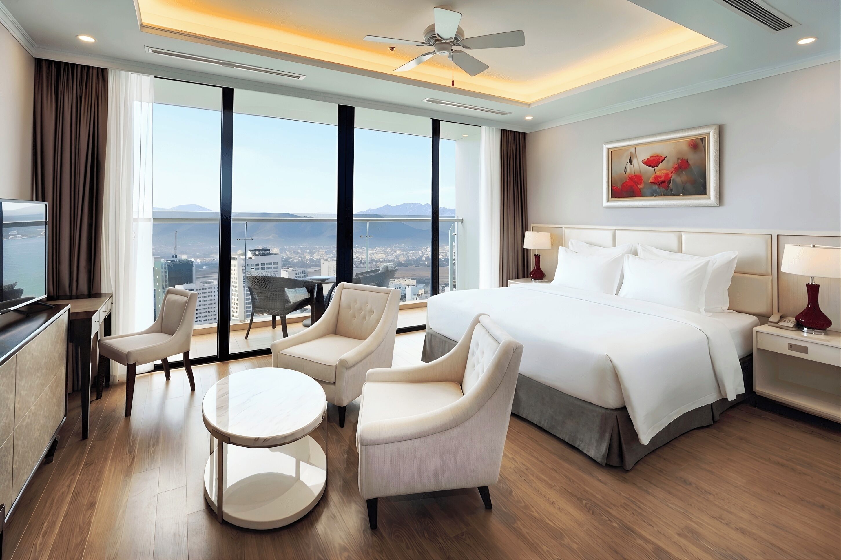Habitación de hotel con cama, dos sillones, una mesita, televisor y ventana grande con vista a la ciudad.