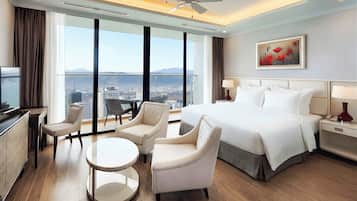 Habitación de hotel con cama, dos sillones, una mesita, televisor y ventana grande con vista a la ciudad.