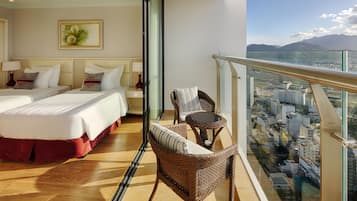 Habitación de hotel con dos camas, un balcón con mobiliario de mimbre y vistas a la ciudad.