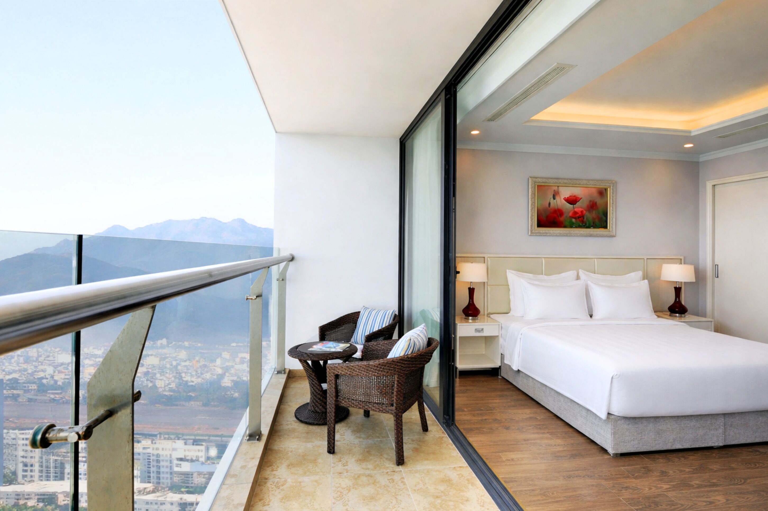 Une chambre d’hôtel avec un balcon, un lit, une table de chevet, une chaise et un tableau.