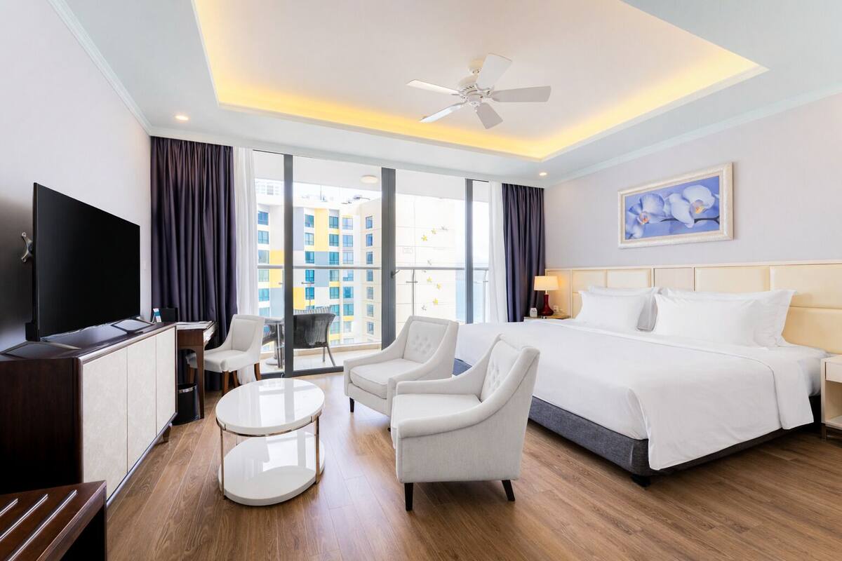 Een hotelkamer met een bed, een televisie, een bureau, een stoel, een klein tafeltje en een plafondventilator.