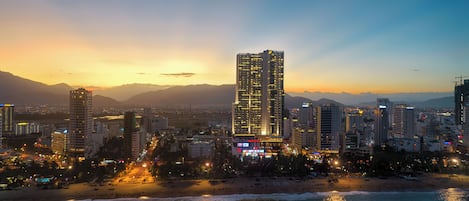 A coastal cityscape with high-rise buildings, a beach, and a sunset.