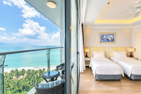 A hotel room with two beds, a balcony with a table and chairs, and a view of the ocean.