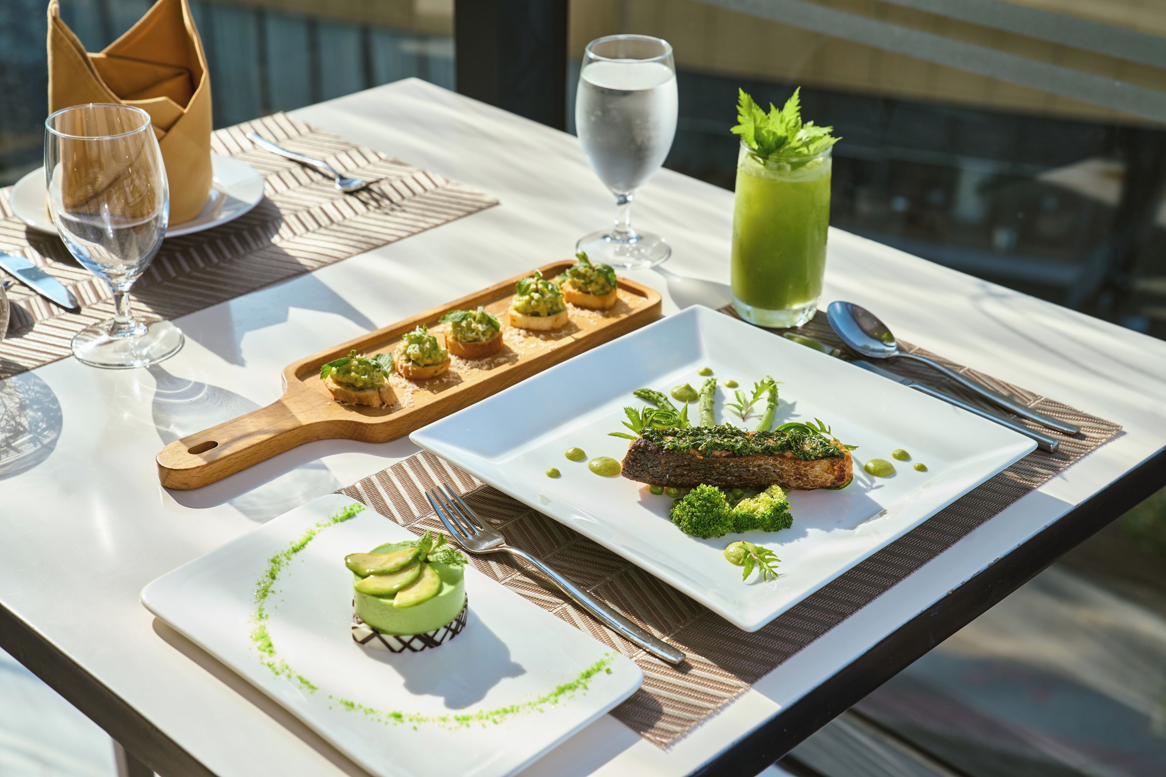 A dining table with a variety of dishes, including a green dessert, a meat dish with greens, and a green drink.