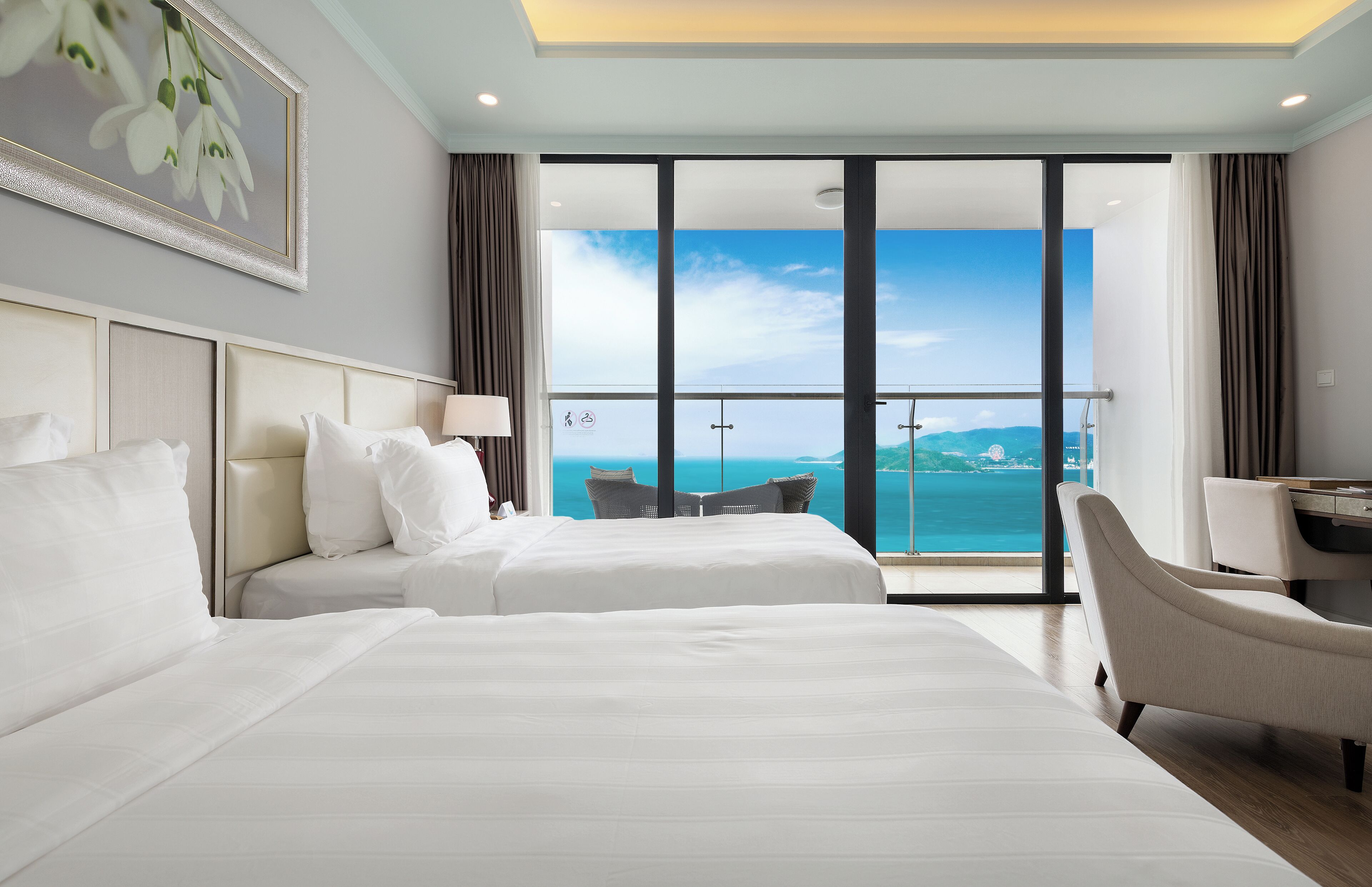 Habitación de hotel con dos camas, un escritorio, una silla y un ventanal con vista al mar.