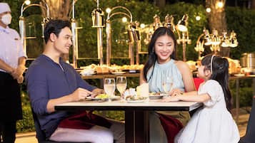 A dining table set outdoors with a waiter, a man, a woman, and a child.